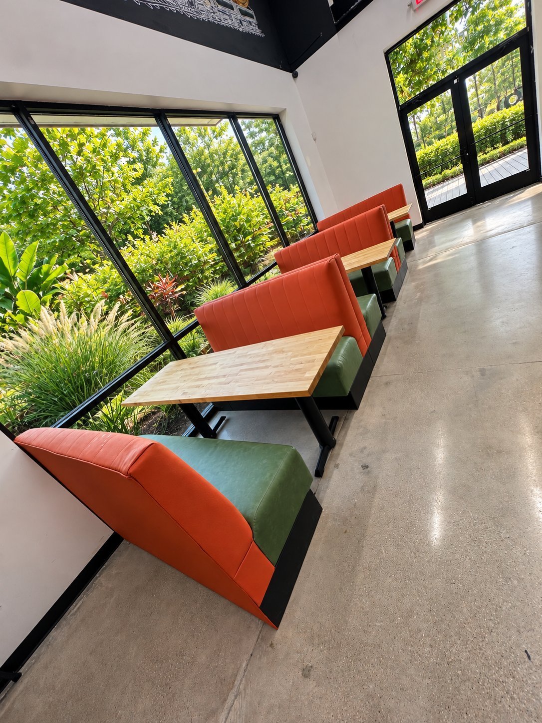 Orange and green leather restaurant booths with light wood tables beside floor-to-ceiling windows