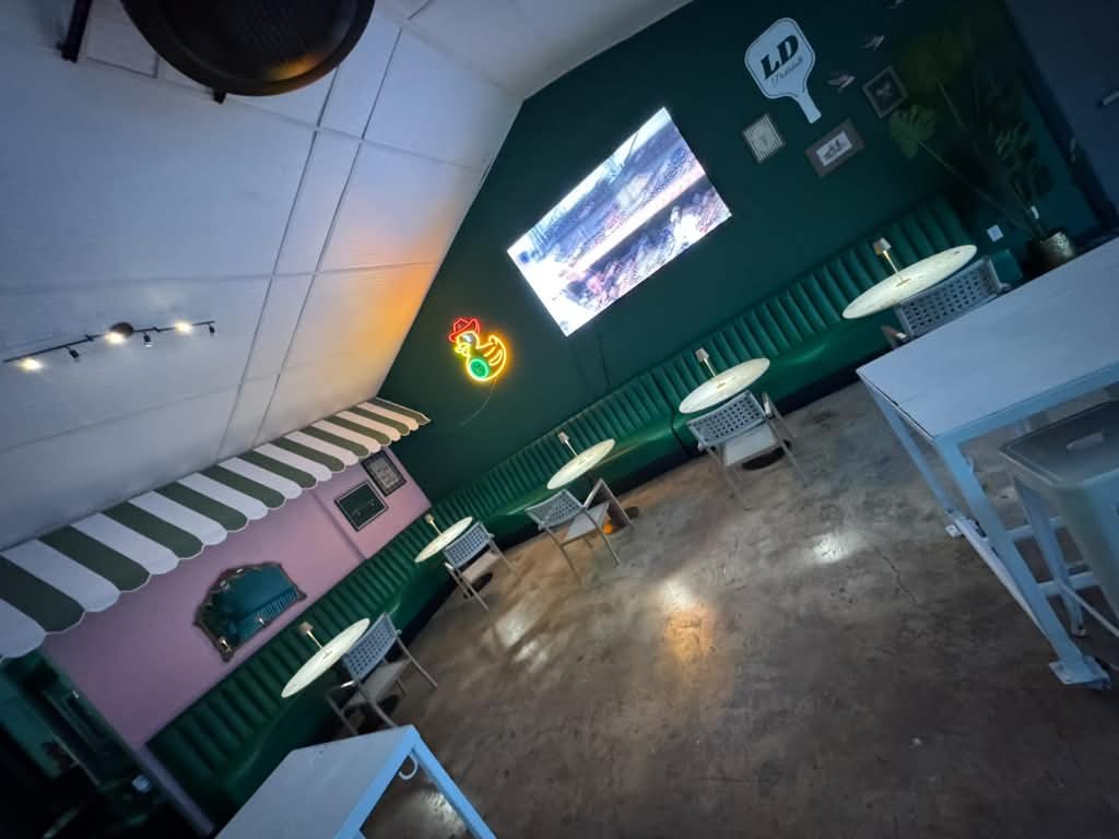 Dark green channel-stitch banquette in sports bar with neon chicken sign and projection screen
