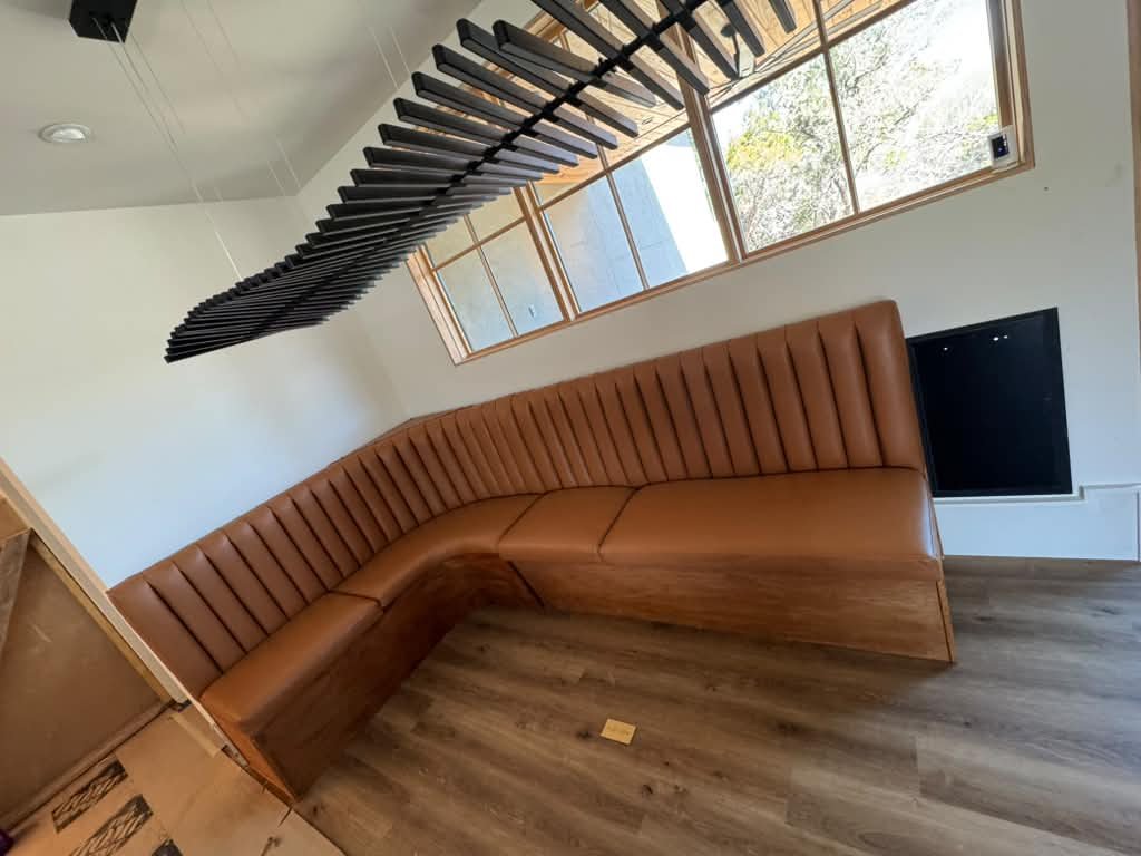Large L-shaped cognac leather channel-stitch banquette in modern restaurant with skylights