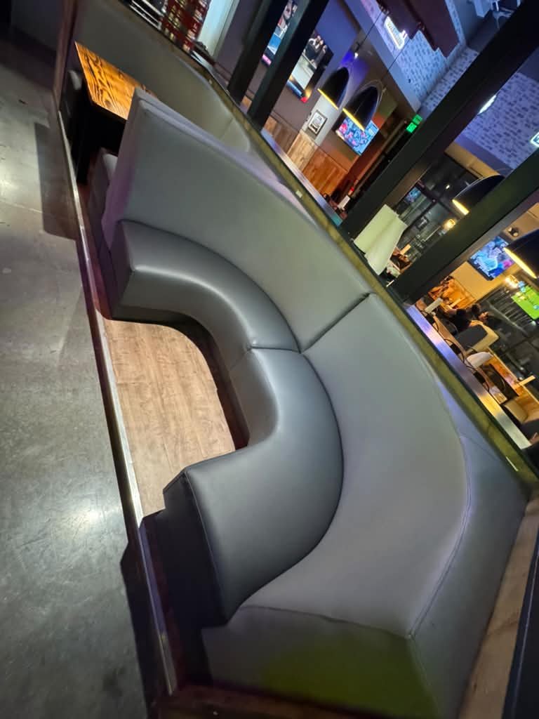 Grey serpentine-form bar booth seating with colorful neon bar backdrop