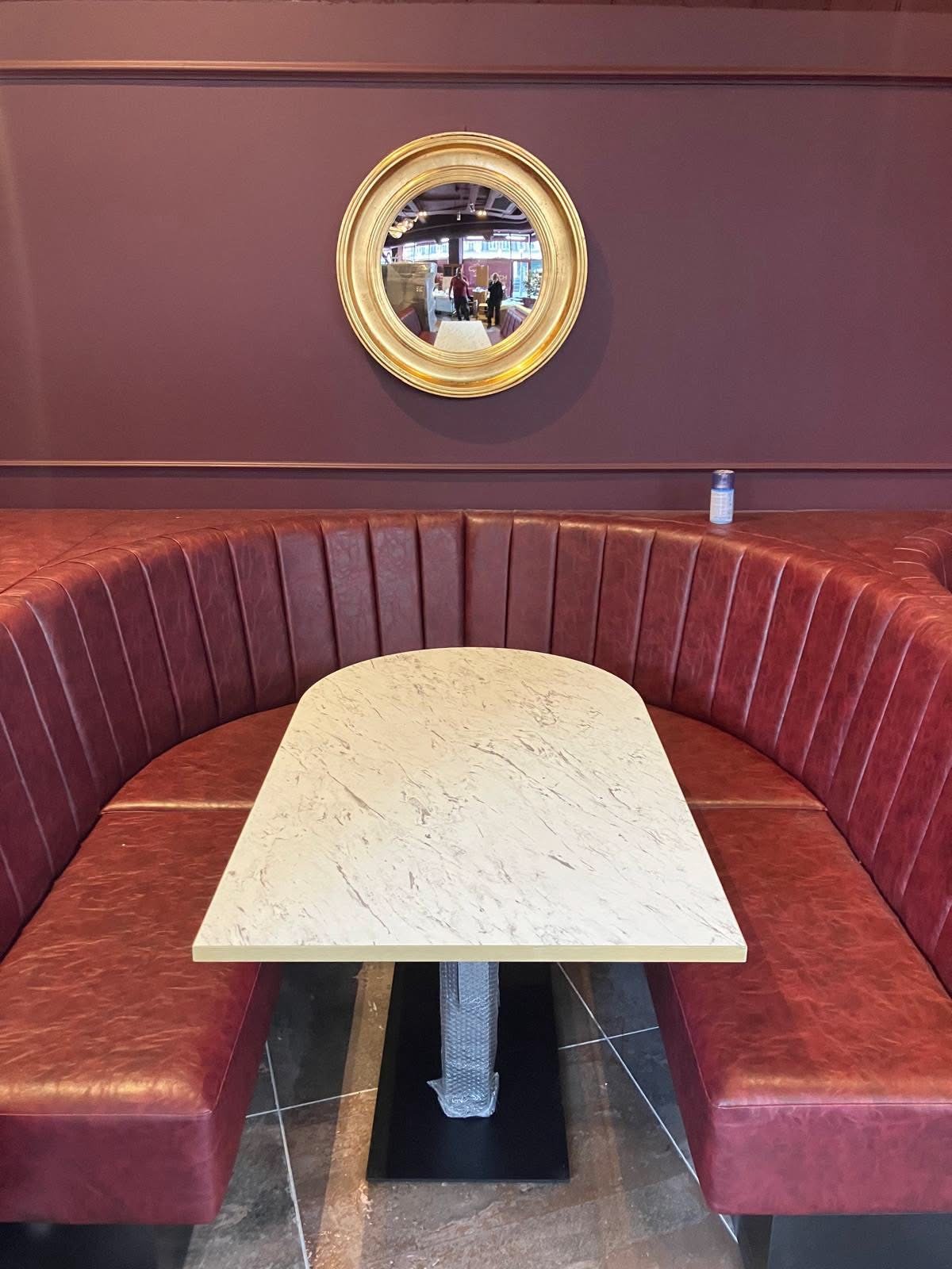 Curved burgundy leather channel-tufted booth with marble arch table and gold convex mirror